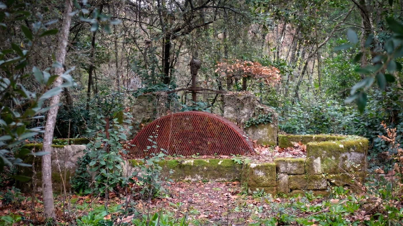 Ancienne pompe à eau en fer forgé, oubliée dans le parc, avec une pierre gravée d'une date ancienne