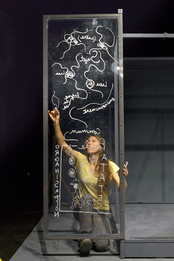 Performeur dans une installation vitrée couverte d'inscriptions, œuvre « Nous qui habitons vos ruines »